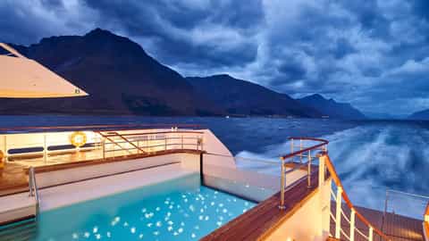 A ship's pool deck overlooks mountains and water at dusk - Le Champlain, Ponant Cruises