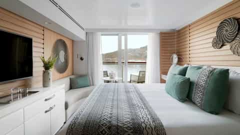 A modern suite bedroom with a balcony overlooking water and mountains - Le Champlain, Ponant Cruises