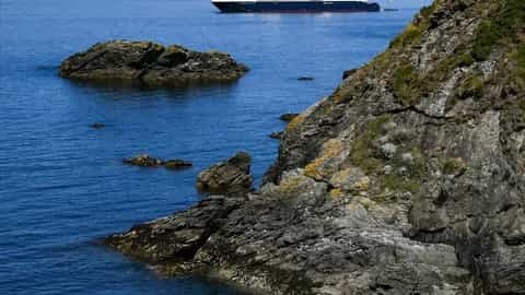 A cruise ship sails on the ocean near a rocky coastline - Le Jacques Cartier, Ponant Cruises