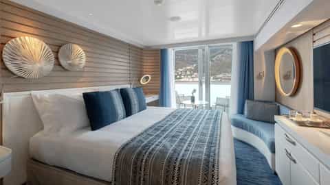 A modern suite with a bed and balcony overlooking a town - Le Laperouse, Ponant Cruises