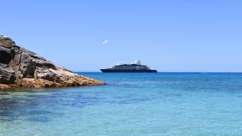 A cruise ship sails on a clear blue sea near a rocky island - Le Lyrial, Ponant Cruises