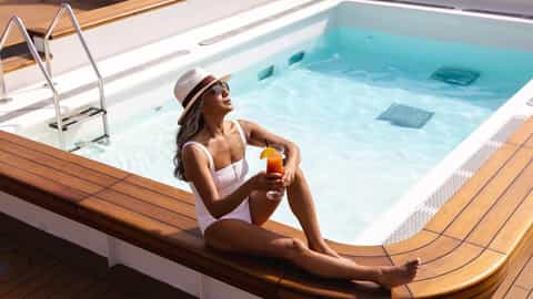 A woman in a swimsuit relaxes by a pool with a drink - Le Soleal, Ponant Cruises