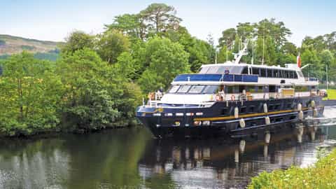 A ship travels down a canal surrounded by trees - Lord of the Glens, Lindblad Expeditions
