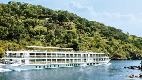 A river ship sails past a lush, tree-covered hillside - ms Amalia Rodrigues, CroisiEurope