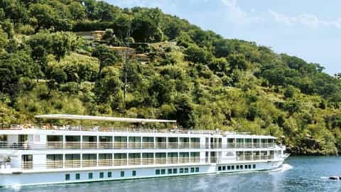A river ship cruises on a calm river with tree-covered hills - ms Amalia Rodrigues, CroisiEurope