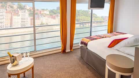 A suite with a bed, champagne, and river view - ms Camargue, CroisiEurope