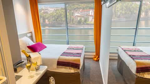 A river cruise cabin with two beds and a view of a city - ms Camargue, CroisiEurope