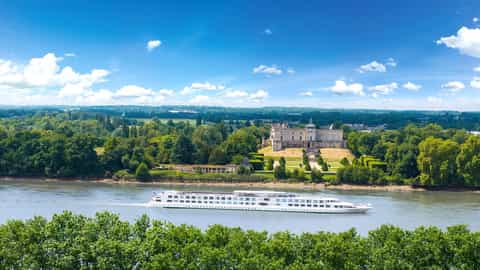 A river ship sails past a chateau on a sunny day - ms Cyrano de Bergerac, CroisiEurope