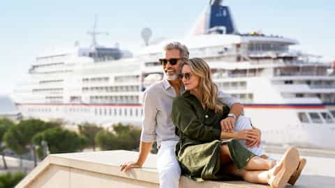 A couple sits together with a cruise ship behind them - ms Europa, Hapag-Lloyd Cruises