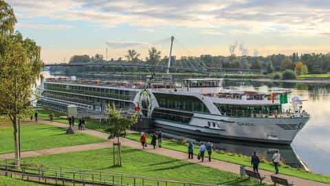 A river cruise ship is docked by a grassy park - MS Grace, Riviera Travel