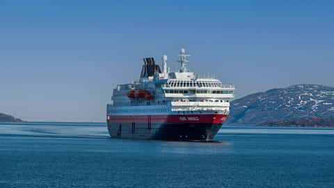 A large ship sails on the water near snow-capped mountains - MS Kong Harald, Hurtigruten