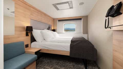 A cabin with a bed, sofa, and a window view - MS Kong Harald, Hurtigruten