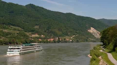 A river ship sails past a green, hilly landscape - ms L'Europe, CroisiEurope