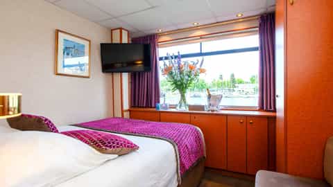 A river view from a ship's cabin with a bed and TV - ms La Belle de Cadix, CroisiEurope