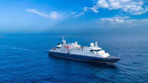 A ship sails on a calm blue ocean under a cloudy sky - ms La Belle des Oceans, CroisiEurope