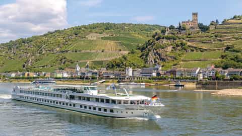 A river cruise ship sails past a town with vineyards and a castle - ms Leonard de Vinci, CroisiEurope