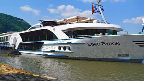 A modern river cruise ship docked on a waterway - MS Lord Byron, Riviera Travel