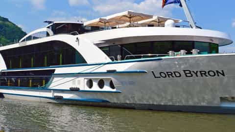 A modern river boat is docked on a calm river - MS Lord Byron, Riviera Travel