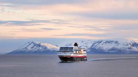 A ship sails on the water with snowy mountains in the background - MS Midnatsol, Hurtigruten
