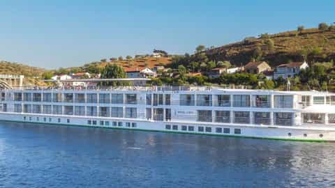 A white river ship sails on blue water near a bridge - MS Miguel Torga, CroisiEurope