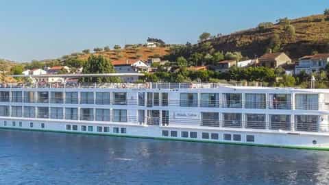 A white river ship sails on blue water near a bridge - MS Miguel Torga, CroisiEurope