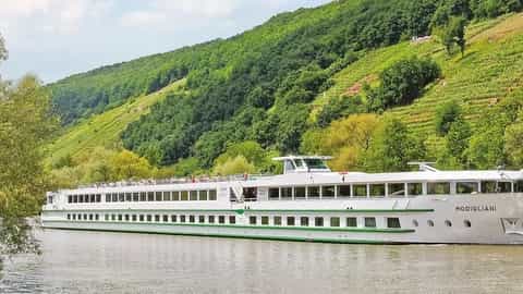 A river cruise ship sails past green hills - ms Modigliani, CroisiEurope
