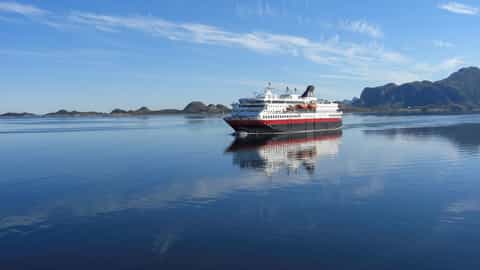 A ship sails on calm blue water with mountains in the background - MS Nordkapp, Hurtigruten