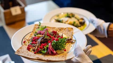 A server presents a flatbread with meat and berries - MS Nordlys, Hurtigruten