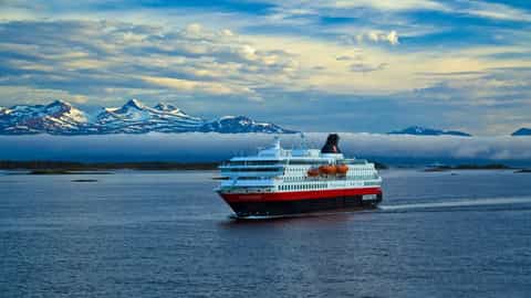 A ship sails past snow-capped mountains under a cloudy sky - MS Nordnorge, Hurtigruten