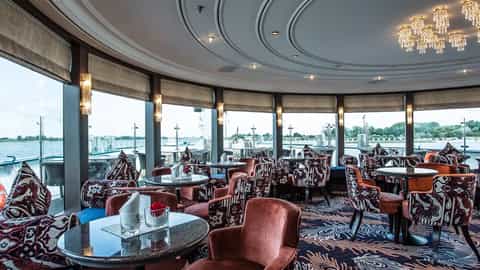 A lounge with seating and tables by a river view - MS Oscar Wilde, Riviera Travel