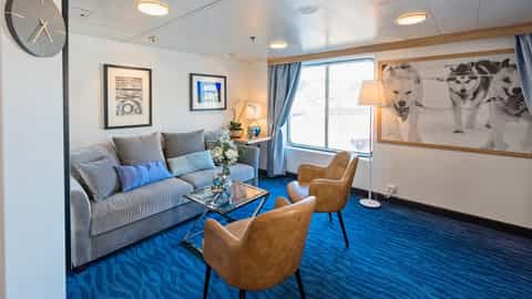 A suite living room with a sofa, chairs, and a large window - MS Polarlys, Hurtigruten