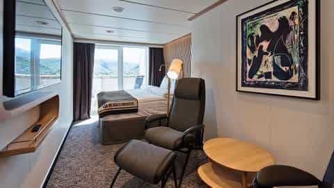A suite bedroom with a bed, seating area, and balcony view - MS Roald Amundsen, HX Expeditions