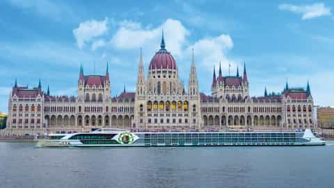 A river ship sails past a grand parliament building - MS Savor, Riviera Travel