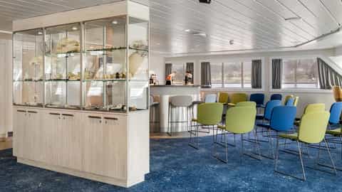 A room with display cases, a bar, and chairs - MS Spitsbergen, HX Expeditions