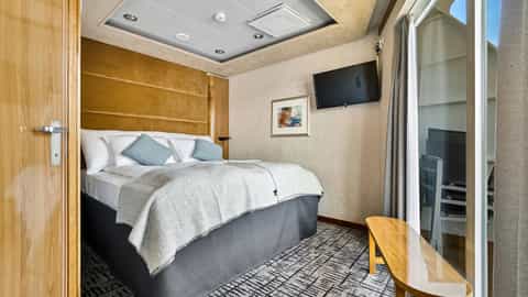 A neatly made bed with blue pillows and a light blanket - MS Trollfjord, Hurtigruten
