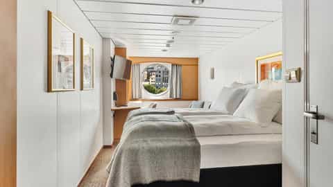 A cabin with two beds and a round window - MS Trollfjord, Hurtigruten