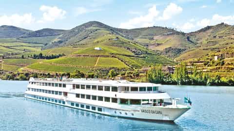 A white river ship sails on blue water near green hills - ms Vasco de Gama, CroisiEurope