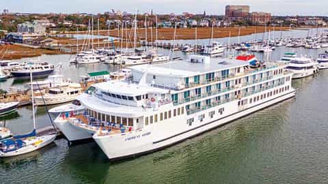 A large white river ship is docked in a marina - ACL American Glory, American Cruise Lines