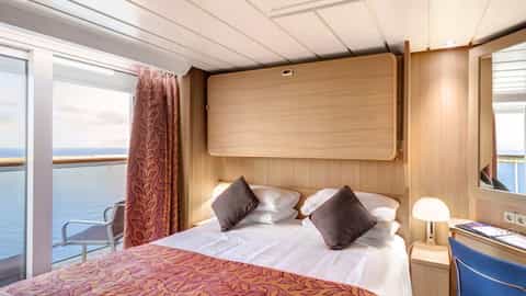 A cabin with a bed and a balcony overlooking the sea - MSC Sinfonia, MSC Cruises
