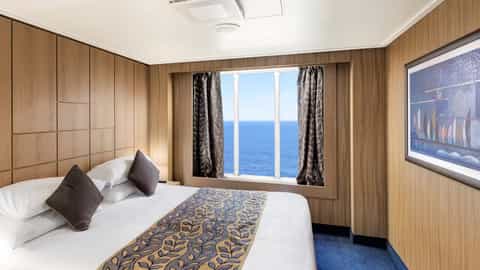 A stateroom with a bed and a large window overlooking the ocean - MSC Sinfonia, MSC Cruises