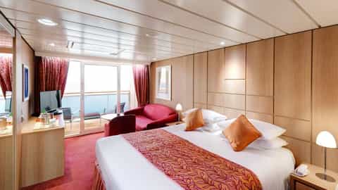 A suite with a bed, sofa, and balcony overlooking the sea - MSC Sinfonia, MSC Cruises