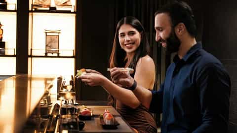 A couple enjoys sushi at a bar with wine - MSC World America, MSC Cruises