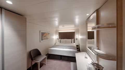 A well-appointed cruise ship cabin with a bed and seating - MSC World Europa, MSC Cruises