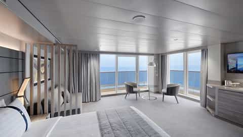 A spacious suite with a bed, seating area, and balcony - MSC World Europa, MSC Cruises