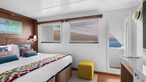A cabin with a bed and a view of the sea and land - National Geographic Delfina, Lindblad Expeditions
