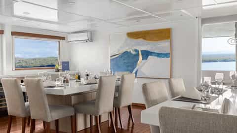 A dining room with set tables and a large window view - National Geographic Delfina, Lindblad Expeditions