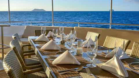 A set dining table on a deck overlooking the ocean - National Geographic Delfina, Lindblad Expeditions