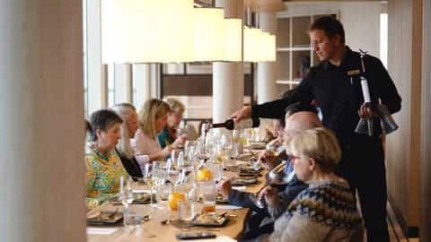 A waiter pours wine for guests at a long dining table - National Geographic Endurance, Lindblad Expeditions