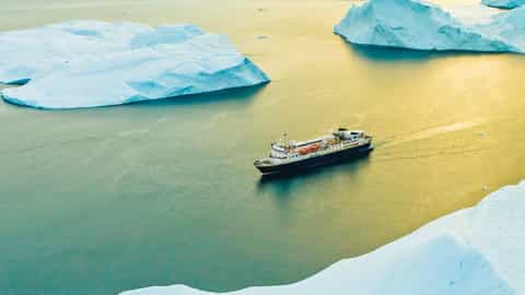 A ship sails through icy waters with large icebergs - National Geographic Explorer, Lindblad Expeditions