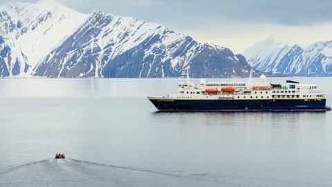 A ship sails on the water near snow-capped mountains - National Geographic Explorer, Lindblad Expeditions